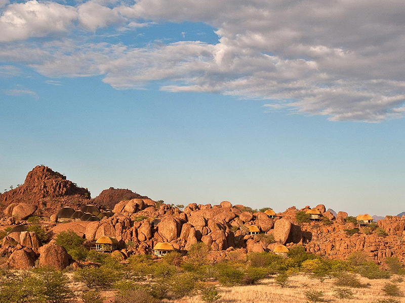 Thatched camp structures tucked between huge red granite boulders in the arid Damaraland landscape, Namibia