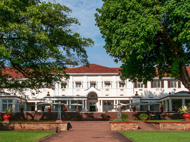 The white colonial-era façade of the Victoria Falls Hotel behind a lawn, garden path and shaded terrace, Zimbabwe