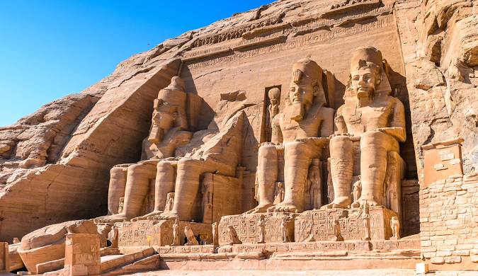 The rock-cut façade of the Abu Simbel temple with seated colossal pharaoh statues carved into the sandstone cliff, Upper Egypt