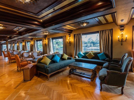 Wood-panelled lounge interior on a Nile cruise vessel in Egypt with armchairs, sofas and windows facing the riverbank