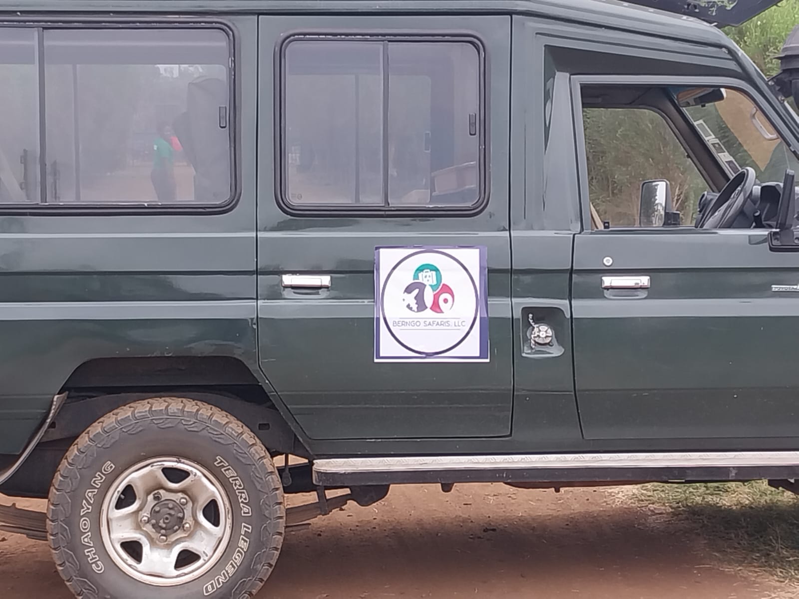 Side view of a green safari Land Cruiser in Kenya displaying a Berngo Safaris, LLC branded door sign
