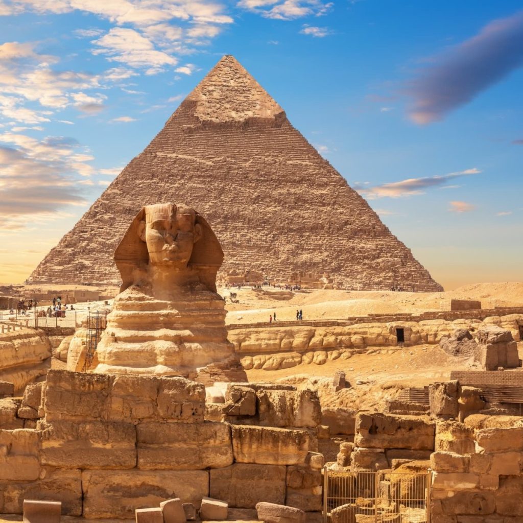 The Great Sphinx of Giza in front of a large pyramid under a blue sky with scattered cloud, Egypt