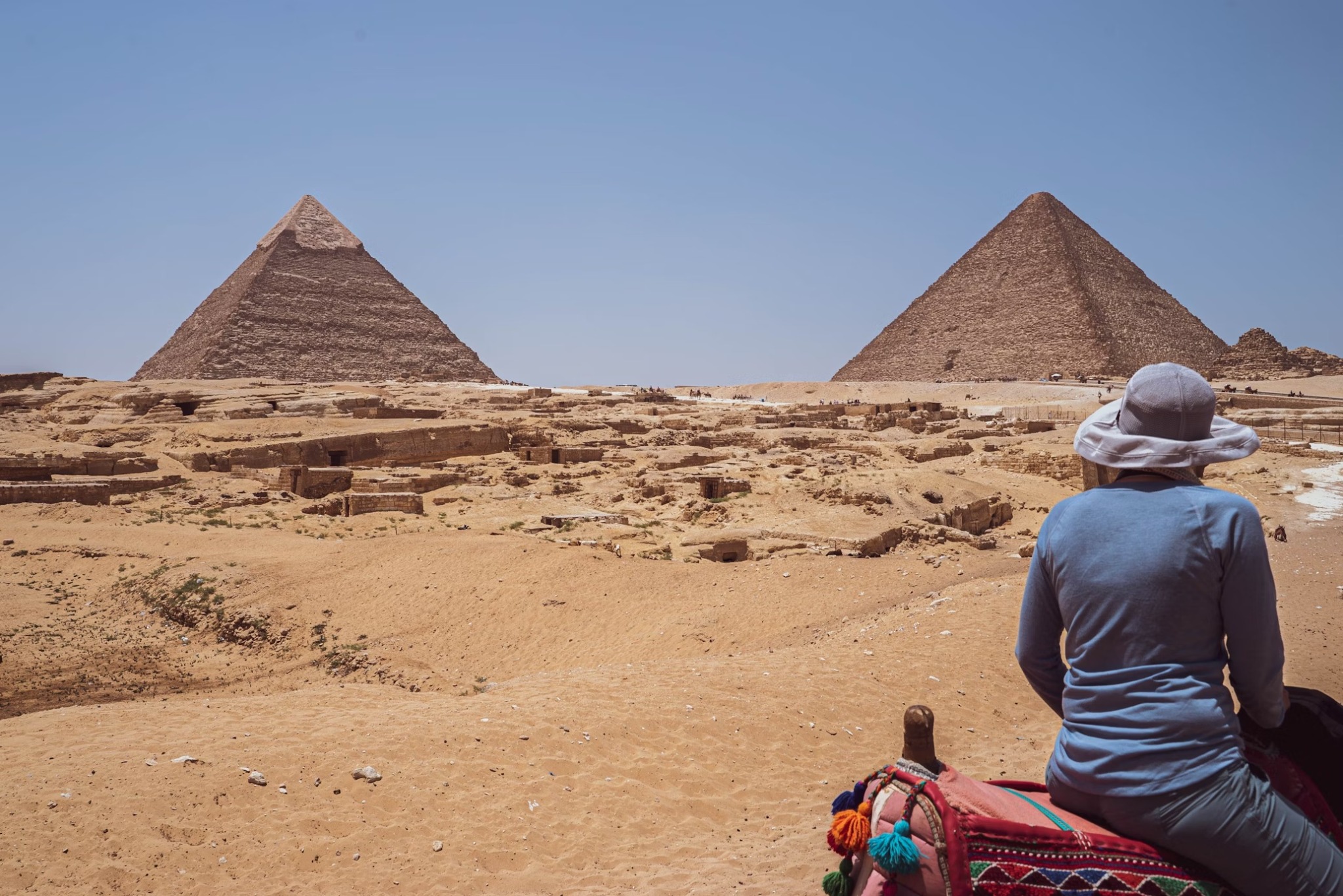A traveller in a sun hat seated on a camel looking across the desert towards two Giza pyramids, Egypt